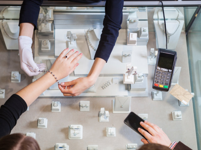 Young woman trying on golden bracelet, man going to pay with cre