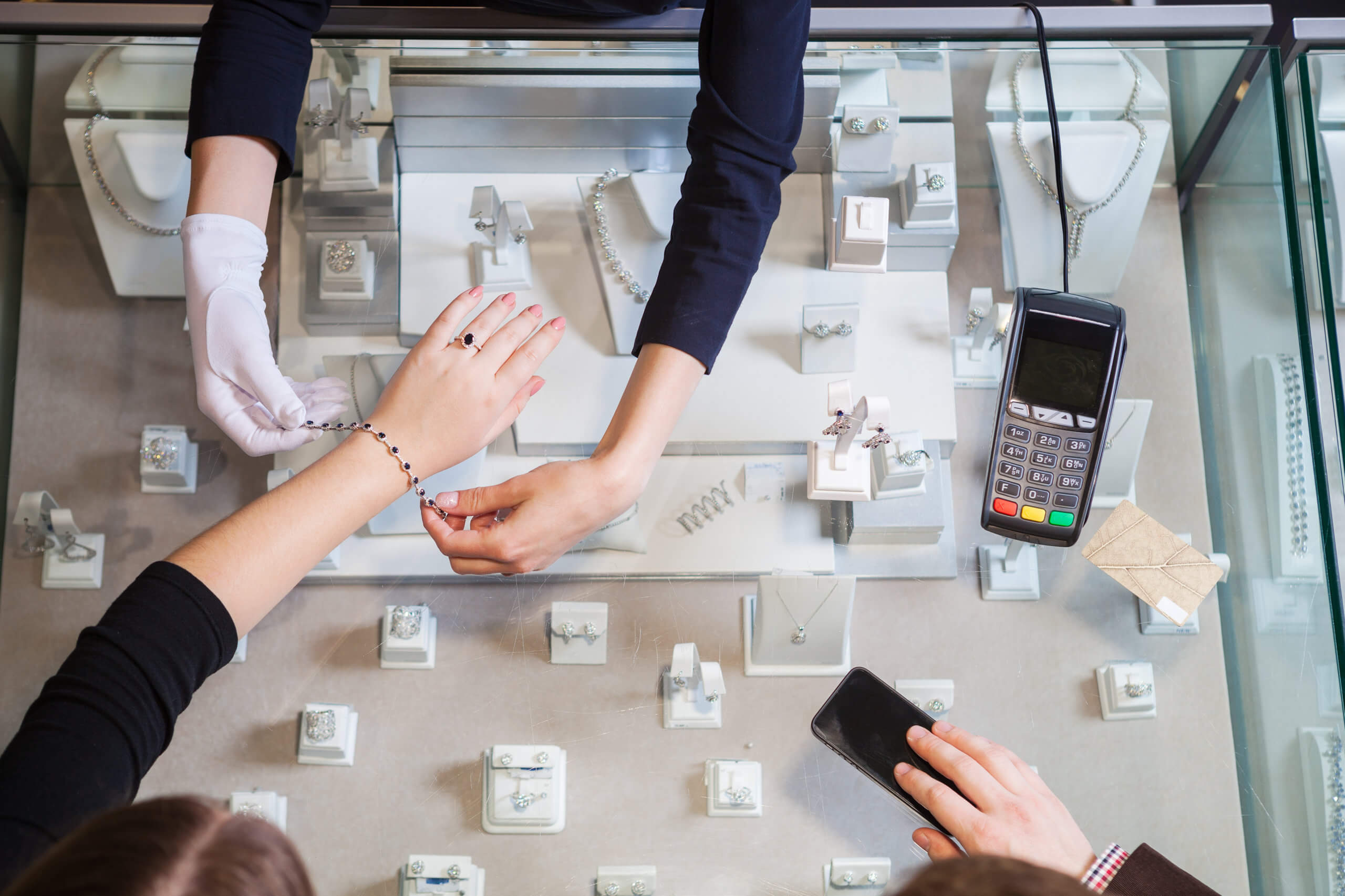 Young woman trying on golden bracelet, man going to pay with cre