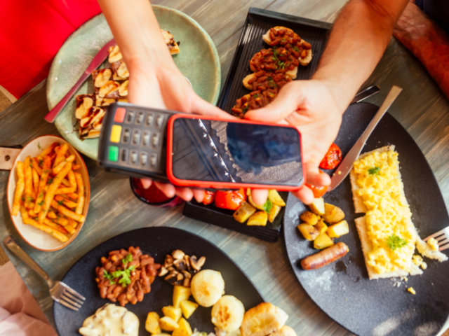 indian man paying in restaurant by credit card app on smartphone reader